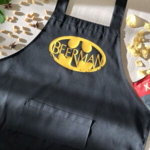 На даному зображенні представлений фартух з веселим принтом "Beerman". Фартух має чорний колір і виготовлений з якісного матеріалу. На фартушку зображено зелень та напис "Beerman". Фартух має регульовані зав'язки на шиї та поясі, що дозволяє налаштувати його під потрібний розмір. Цей фартух стане відмінним подарунком для тих, хто любить готувати та прикрашати свій дім.