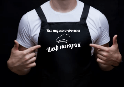 На даному зображенні представлений фартух з веселим принтом "Шеф на кухні". Фартух має чорний колір і виготовлений з якісного матеріалу. На фартушку зображено кухонні прилади, зелень та напис "Шеф на кухні". Фартух має регульовані зав'язки на шиї та поясі, що дозволяє налаштувати його під потрібний розмір. Цей фартух стане відмінним подарунком для тих, хто любить готувати та прикрашати свій дім.