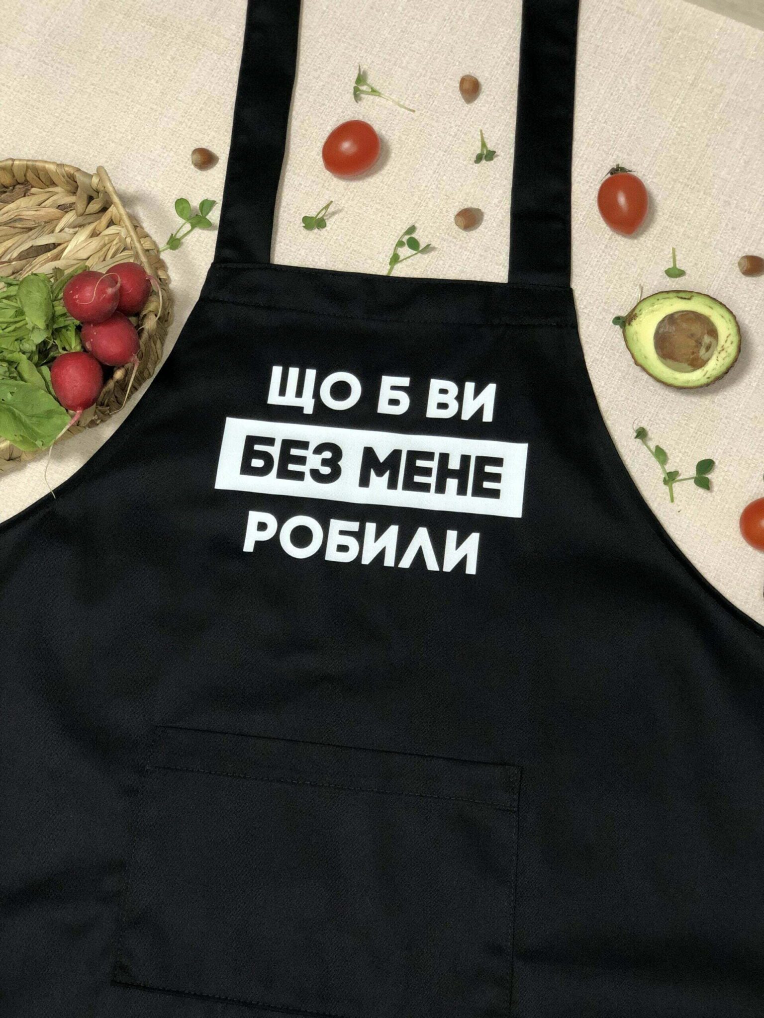 На даному зображенні представлений фартух з веселим принтом "Що б ви без мене робили". Фартух має чорний колір і виготовлений з якісного матеріалу. На фартушку зображено кухонні прилади, зелень та напис "Що б ви без мене робили". Фартух має регульовані зав'язки на шиї та поясі, що дозволяє налаштувати його під потрібний розмір. Цей фартух стане відмінним подарунком для тих, хто любить готувати та прикрашати свій дім.
