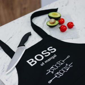 На даному зображенні представлений фартух з веселим принтом "Boss of mangal". Фартух має чорний колір і виготовлений з якісного матеріалу. На фартушку зображено кухонні прилади, зелень та напис "Boss of mangal". Фартух має регульовані зав'язки на шиї та поясі, що дозволяє налаштувати його під потрібний розмір. Цей фартух стане відмінним подарунком для тих, хто любить готувати та прикрашати свій дім.